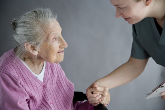 Ältere Frau und Pflegekraft schütteln sich die Hände, freundlich lächelnd.